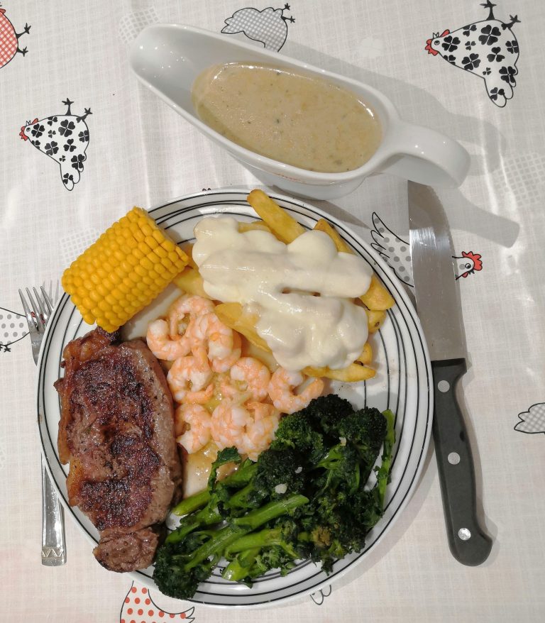 Plate with steak, shrimp, cheesy chips, broccoli, corn on the cob with a side of creamy gravy as my last meal before starting a vegan challenge