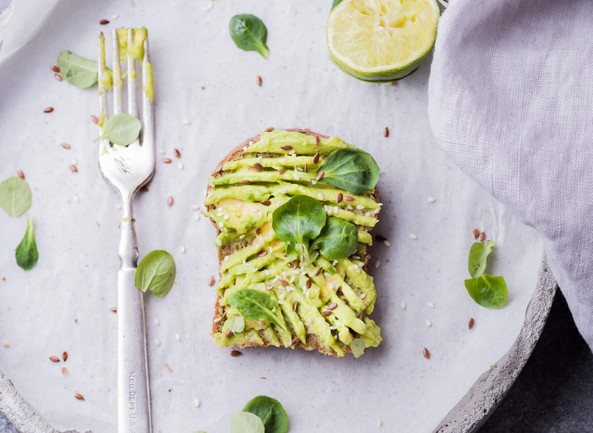 White plate with avocado on toast and half a lime