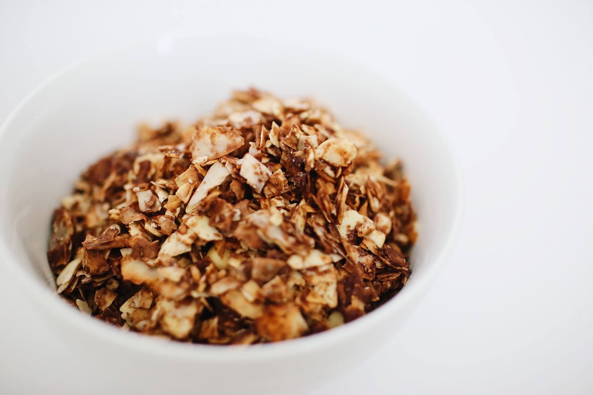 White bowl filled with breakfast granola with a white background