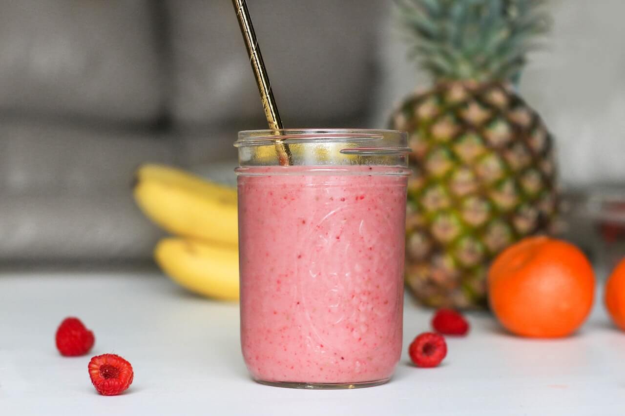Healthy breakfast smoothie in a jam jar with a straw and fruits in the background