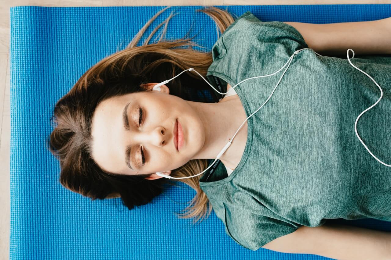 Girl with eyes closed lying on a yoga mat, listening to a guided meditation on headphones