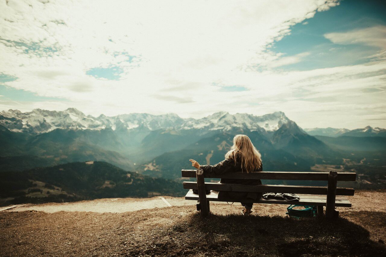 Woman sitting on a bench on a mountain top enjoying the view - practicing mindfulness and living in the moment