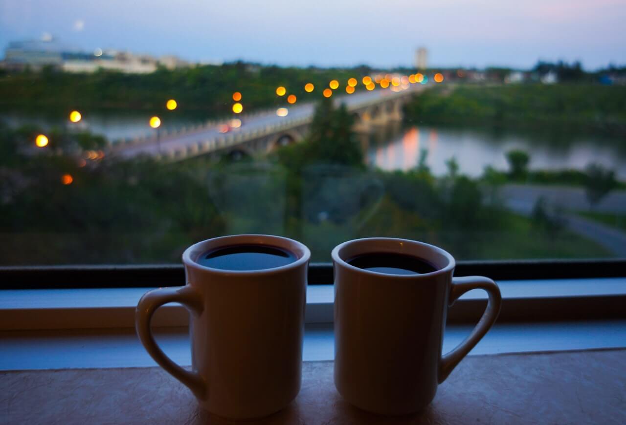 Coffee mugs sitting by window with a view of a bridge