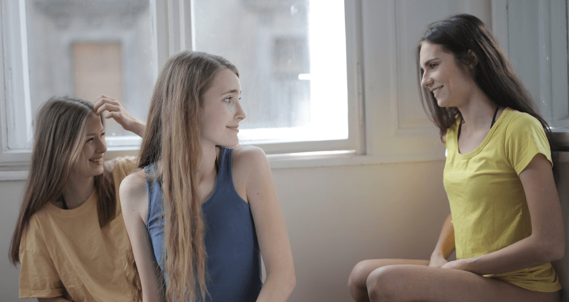 3 happy girls sitting on a bed looking at each other as if having a discussion