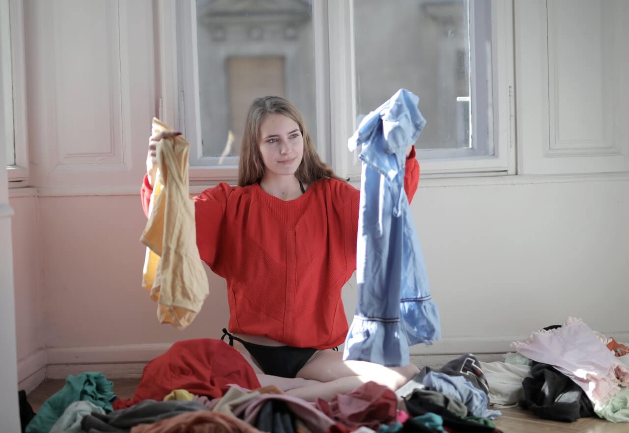 Woman sitting on the floor sorting through clothes while decluttering her wardrobe
