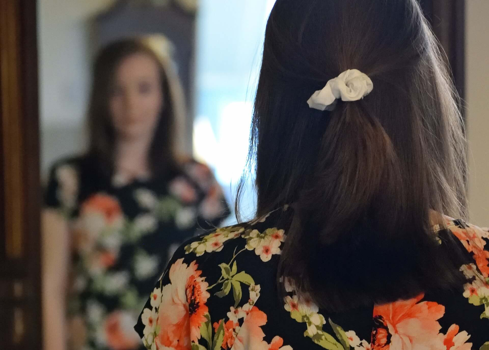 Woman in a dress looking in the mirror with a blurry reflection in the background