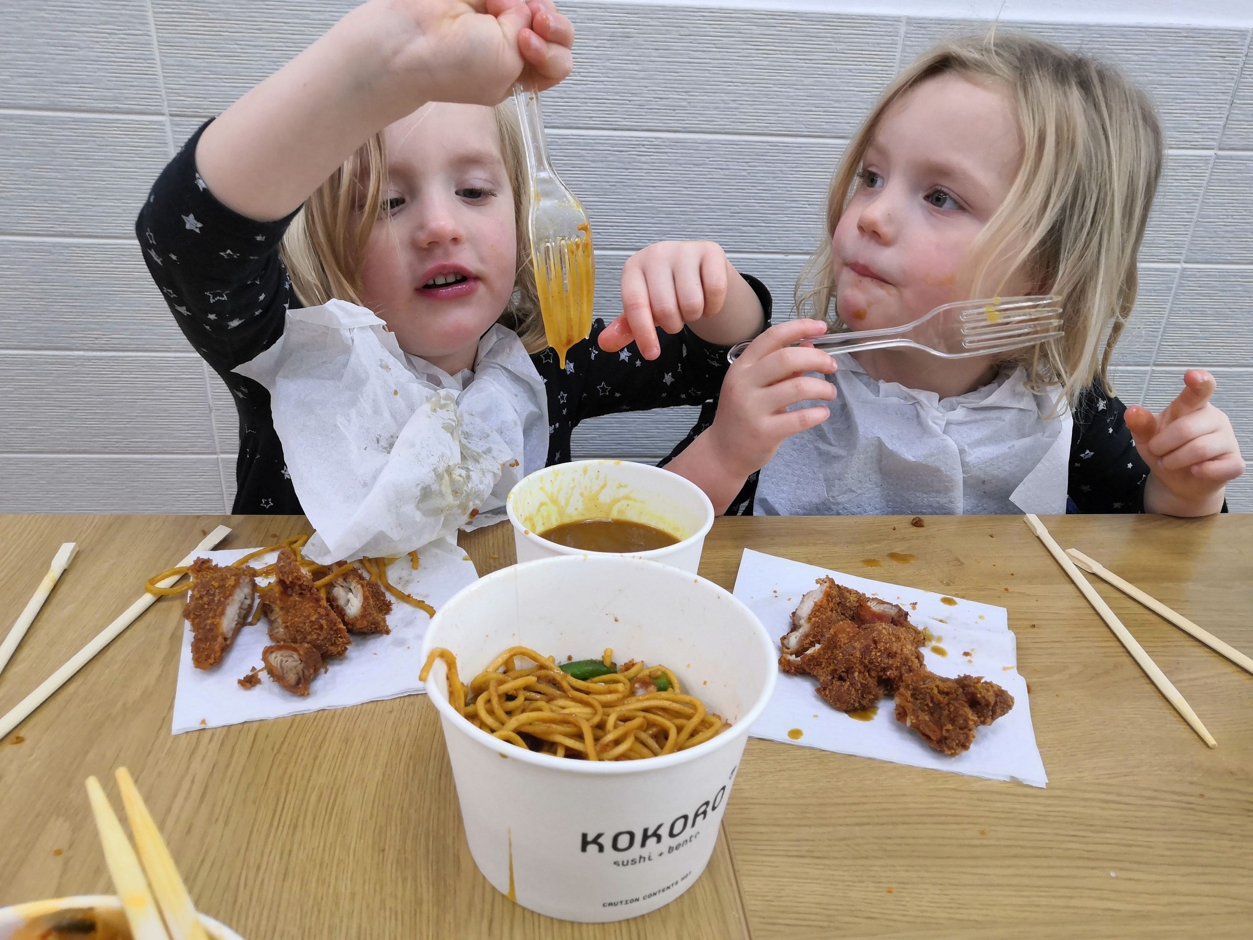 Two young children eating chicken katsu curry at a table.