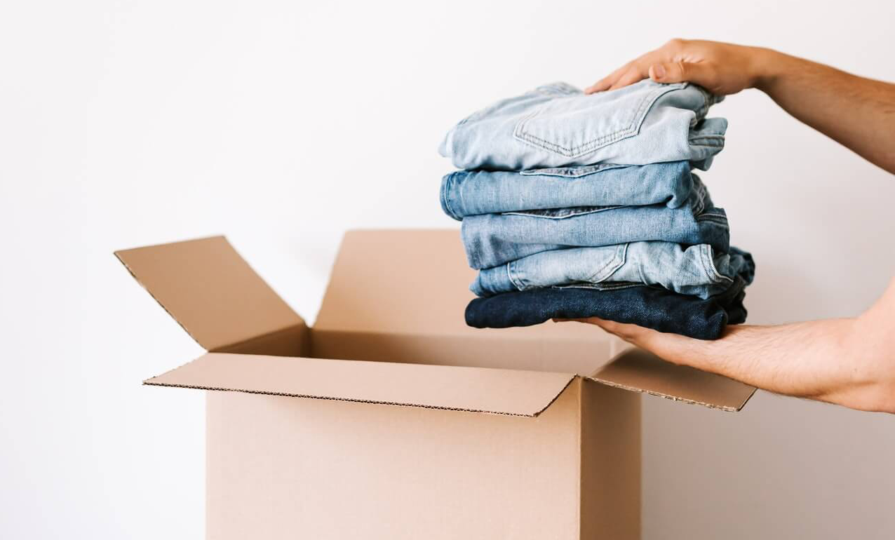 Hands putting a folded pile of jeans in a cardboard box to help declutter a wardrobe