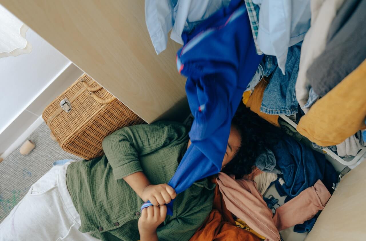 Woman lying on the floor with clothes from wardrobe all over her